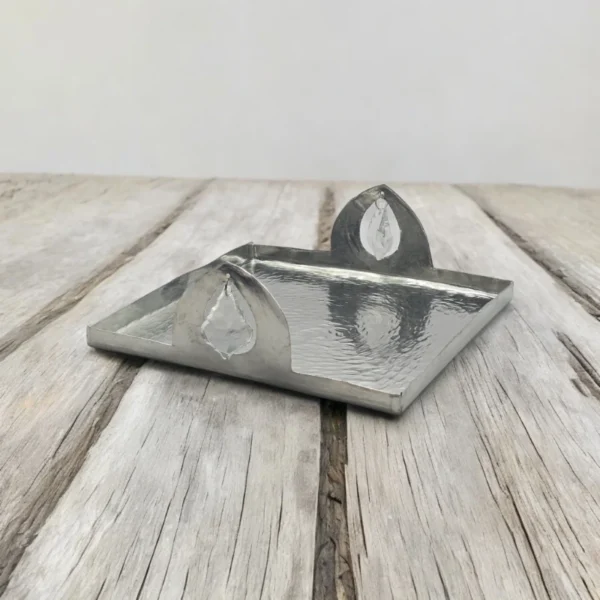 A square, hammered copper tray with a raised edge and two decorative leaf-shaped handles. The tray is sitting on a wooden surface.