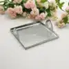 A square, hammered copper tray with a raised edge and two decorative leaf-shaped handles. The tray is sitting on a wooden surface.